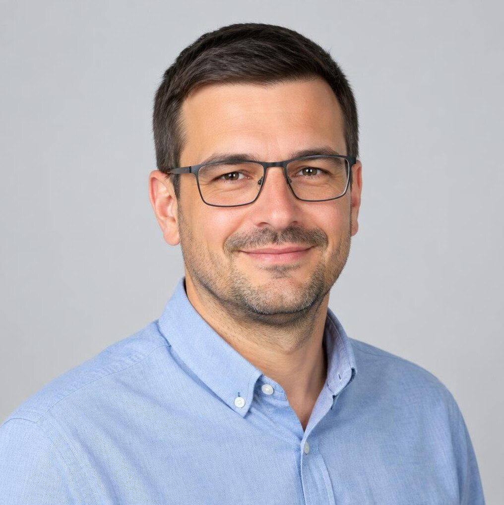 Studio portrait of a man with short dark hair and glasses smiling